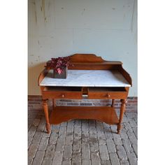 an old wooden desk with marble top and drawer on brick floor next to white wall