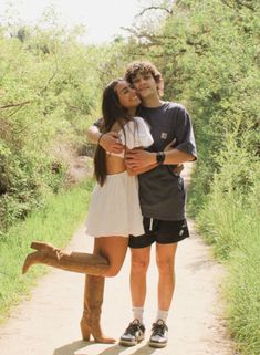 a man and woman hugging each other while standing on a dirt road