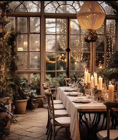 a dining room table is set with white linens and lit candles in front of the windows