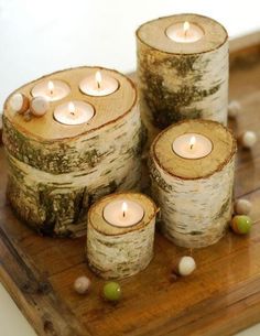 four candles are sitting on a wooden tray next to some beads and wood slices with moss