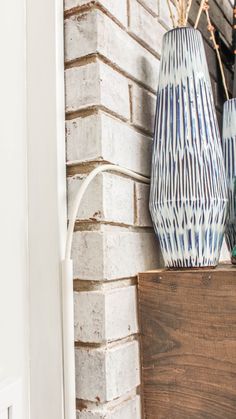 two blue and white vases sitting on top of a wooden box next to a brick wall