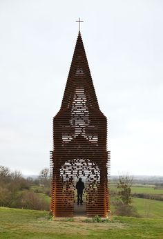 a man standing in front of a church made out of wooden slats and sticks