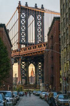 cars are parked on the street in front of tall buildings and a large bridge over it