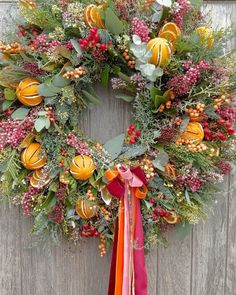 a wreath with oranges, berries and greenery on it hanging on a wooden door