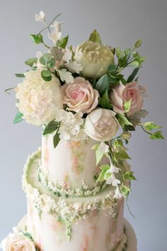 a three tiered cake with flowers and greenery on the top is decorated in white frosting