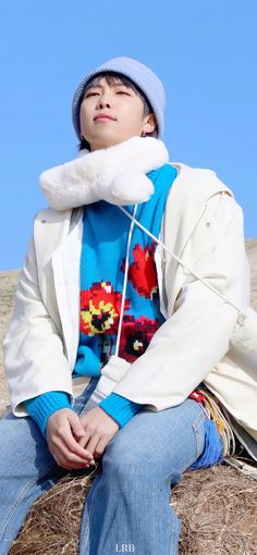 a young man sitting on top of a pile of hay wearing a white jacket and blue hat