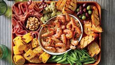 a platter filled with shrimp, corn, beans, and other foods next to wine glasses