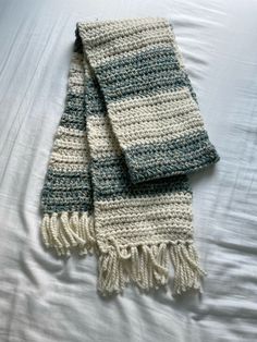 two crocheted scarves laying on top of a white bed sheet with blue and green stripes