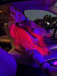 a woman sitting in the passenger seat of a car with her head down and pink hair