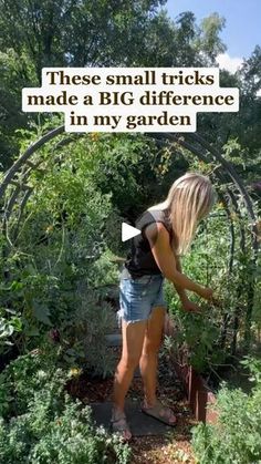 a woman standing in the middle of a garden with her hand on top of some plants