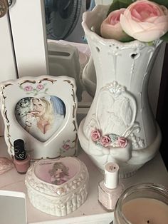 a white vase filled with pink roses next to other items on a table and in front of a mirror