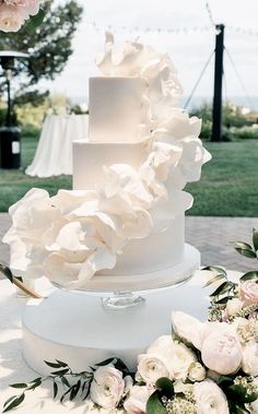 a three tiered white wedding cake sitting on top of a table next to flowers