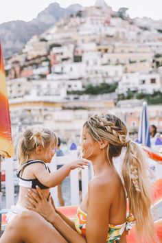 a mother and her daughter sitting on the beach in their bathing suits, both holding each other