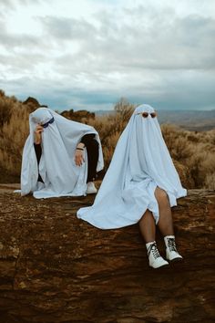 two people dressed in white are sitting on a log and one is covering her face