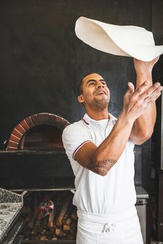 a man in white shirt and apron tossing a frisbee over his head while standing next to an oven