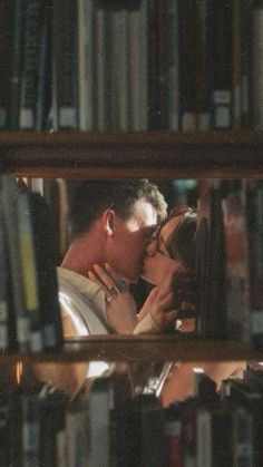 a man and woman kissing in front of a book shelf with many books on it