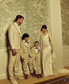 a man and two boys standing next to each other in front of a wallpapered background