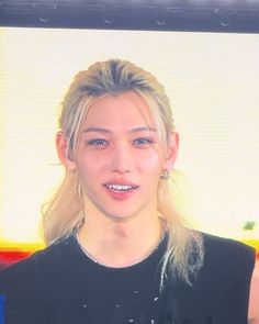 a woman with blonde hair wearing a black shirt and smiling at the camera while standing in front of a television screen