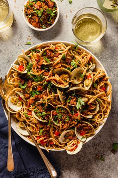 pasta with clams and sauce in a white pan on a gray surface next to two bowls