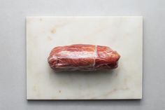 a piece of meat wrapped in plastic sitting on top of a white marble countertop