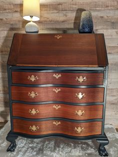 a wooden dresser with black and brown drawers next to a lamp on top of a white rug