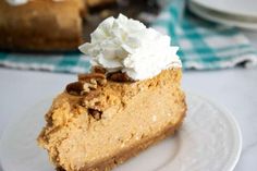 a slice of pumpkin cheesecake with whipped cream on top and pecans in the background