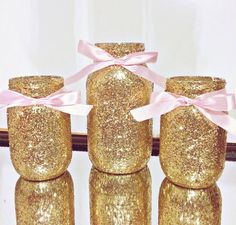 four gold glitter jars with pink bows on them