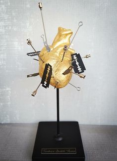 a gold sculpture with scissors and other items on it's stand in front of a white wall