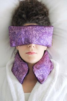 a woman laying in bed with her eyes covered by a purple eye mask that covers her eyes