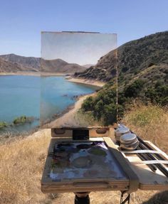 an artist's easel with a painting on it in front of a lake