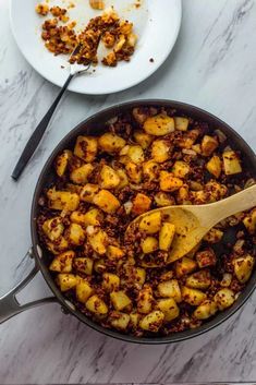 a skillet filled with cooked potatoes on top of a white counter next to a plate of food