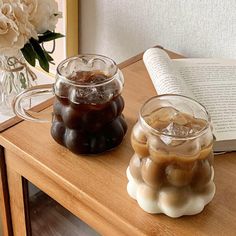 two glasses filled with liquid sitting on top of a table next to an open book