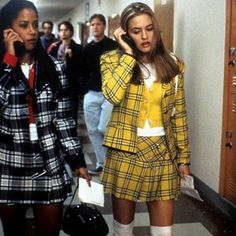 two women in plaid outfits talking on cell phones while others walk down the hallway behind them