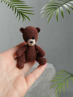 a small crocheted teddy bear sitting on top of a rock next to a plant