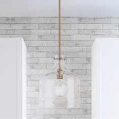 a glass light fixture hanging from the ceiling in a white kitchen with marble tiles on the walls