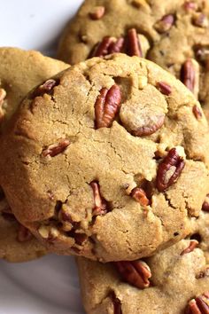 several pecan cookies stacked on top of each other in a white plate with more pecans around them