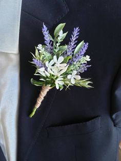 a boutonniere with purple flowers and greenery is seen on the lapel of a man