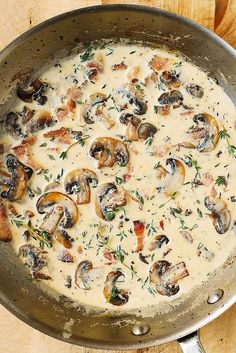 a pan filled with mushrooms and sauce on top of a wooden table