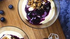 two bowls filled with blueberries and yogurt on top of a wooden cutting board