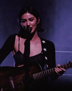 a woman holding a guitar in front of a microphone and singing into a microphone with her right hand