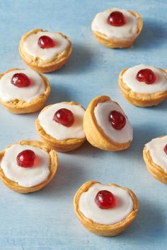 small pastries with white icing and cherries are arranged on a blue surface