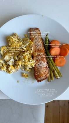 a white plate topped with eggs, asparagus and salmon next to carrots