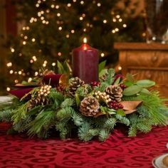 a christmas centerpiece with pine cones, berries and greenery on a red table cloth