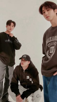 three young men standing next to each other in front of a white wall wearing black sweatshirts