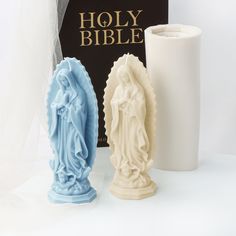 two statues next to a book and candle holder