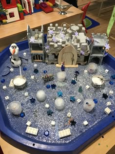 a blue tray filled with lots of toys on top of a wooden table covered in snow