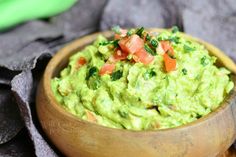 a wooden bowl filled with guacamole and tomatoes