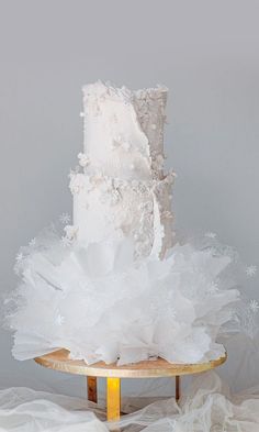 a three tiered white wedding cake sitting on top of a wooden table covered in tulle