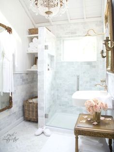 a white bathroom with a chandelier hanging from the ceiling and flowers on the table