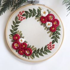 an embroidery hoop with red and white flowers on it next to a christmas tree branch